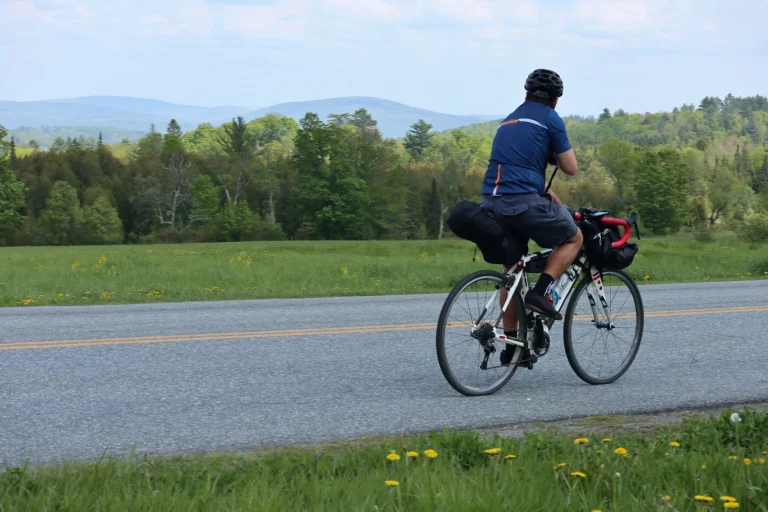 Homme à vélo sur une route de campagne avec des montagnes en arrière-plan (sans visage, regardant au loin, vélo de gravier équipé de sacoches) voyage, tourisme, vélo, cyclisme, bicyclette, vélo